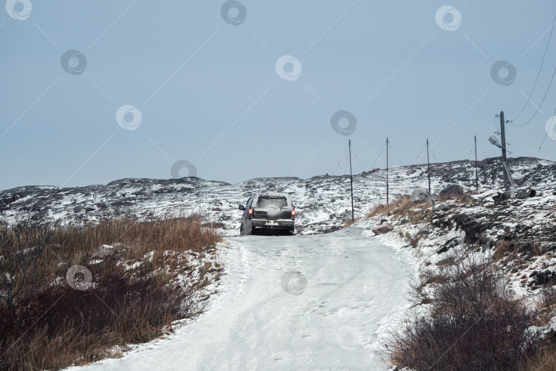 Скачать Автомобиль движется по сложной обледенелой дороге. Скользкая арктическая дорога через холмы фотосток Ozero