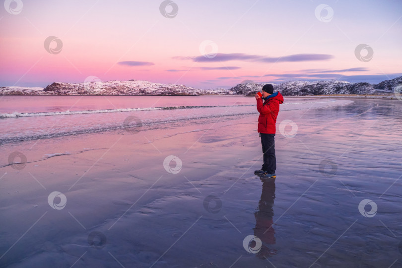 Скачать Чашка горячего чая в руке мужчины на арктическом побережье на фоне заснеженных северных холмов. Чудесный полярный закат. фотосток Ozero