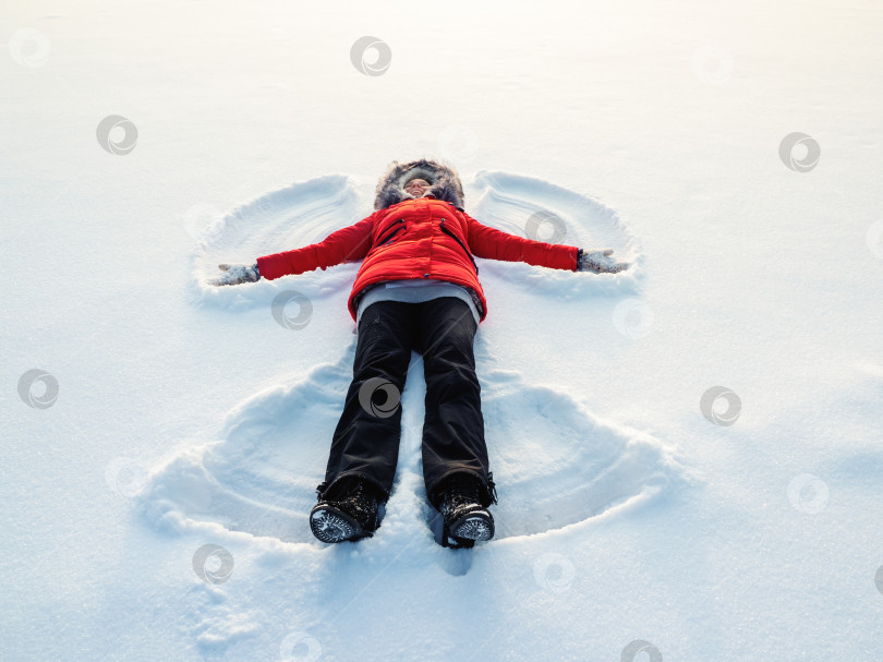 Скачать Снежный ангел, сделанный счастливой женщиной на снегу. Плоский вид сверху фотосток Ozero