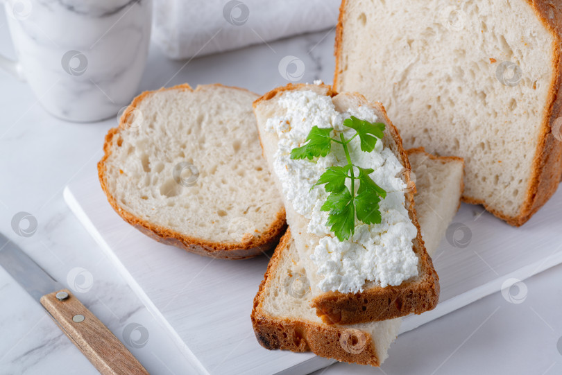 Скачать Домашний хлеб на деревянной разделочной доске с творожным сыром и петрушкой. Украшен зеленью фотосток Ozero