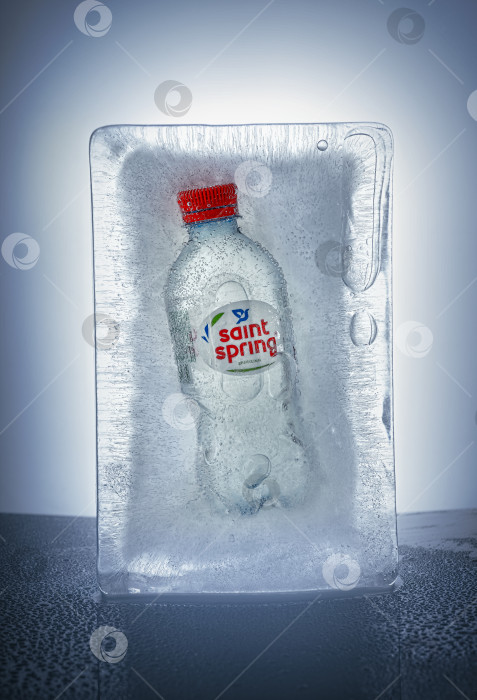 Скачать Ставрополь, Россия, 15 апреля 2022 года: бутылка "Святого источника", замороженная в кусочке льда. Пузырьки и трещины во льду, вертикальное фото фотосток Ozero