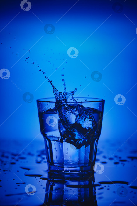 Скачать Кубики льда, падающие в стакан с водой, крупным планом. фотосток Ozero