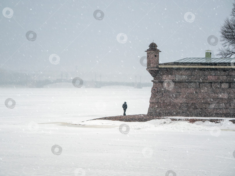 Скачать Одинокий мужчина, идущий позади. Красивый весенний городской пейзаж со снегопадом. Контрастный вид на Петропавловскую крепость зимой. Санкт-Петербург. фотосток Ozero