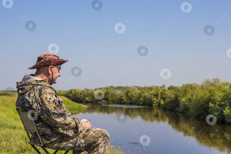 Скачать Рыбак пьет чай и любуется красотой реки в летний день фотосток Ozero