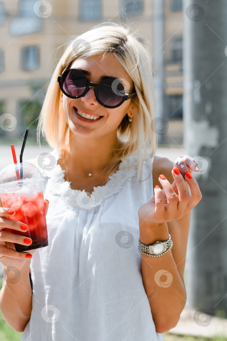 Скачать Девушка держит в руках печенье и стакан свежевыжатого сока. Молодая красивая женщина в солнцезащитных очках улыбается на улице. фотосток Ozero
