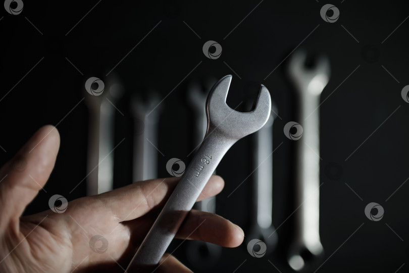Скачать Мужская рука, демонстрирующая комбинированный стальной гаечный ключ на фоне набора профессиональных инструментов. Крупный план фотосток Ozero