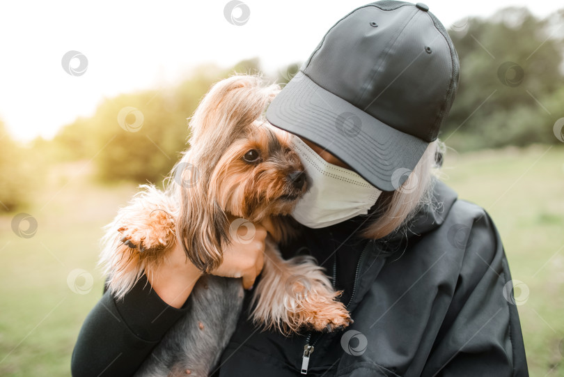 Скачать Выгуливающий йоркширского терьера. Молодая женщина в медицинской маске держит на руках собаку. Новая норма фотосток Ozero