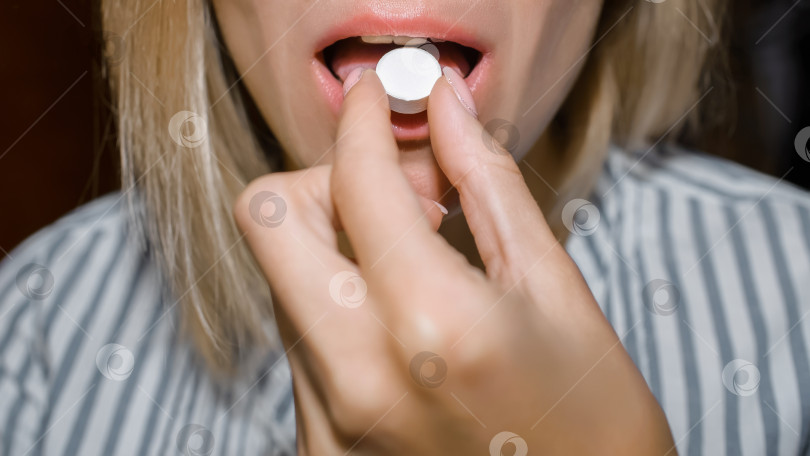 Скачать Женщина кладет таблетку в рот. Молодая женщина принимает лекарство. Укороченные фотосток Ozero