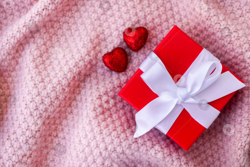 Скачать красная подарочная коробка и два красных блестящих сердечка. на розовом вязаном фоне. рукоделие, вязание, день святого Валентина фотосток Ozero