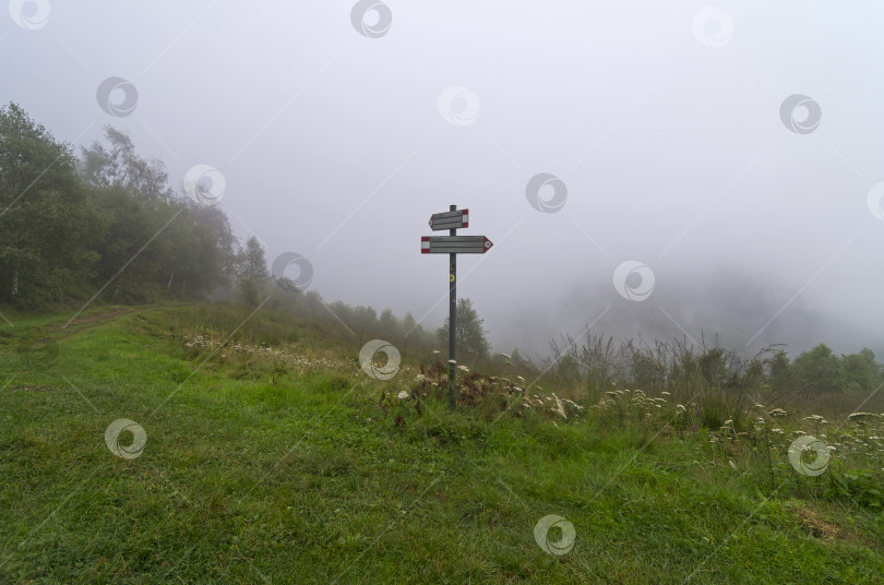 Скачать Указатель на пешеходную тропу в горах, покрытых густым туманом. фотосток Ozero