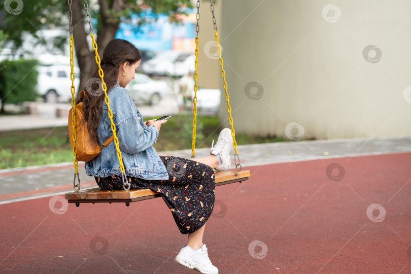Скачать Девушка сидит на качелях и проверяет телефон. Девушка сидит и видеочатит по телефону фотосток Ozero
