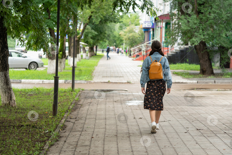 Скачать девочка в платье и джинсовой куртке с оранжевым рюкзаком за плечами идет в школу и оглядывается назад. фотосток Ozero