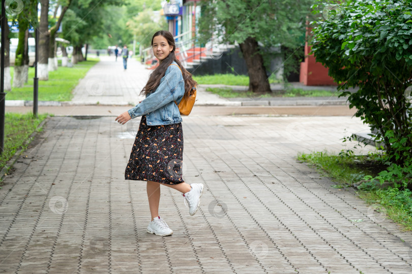 Скачать девочка в платье и джинсовой куртке с оранжевым рюкзаком за плечами идет в школу. фотосток Ozero