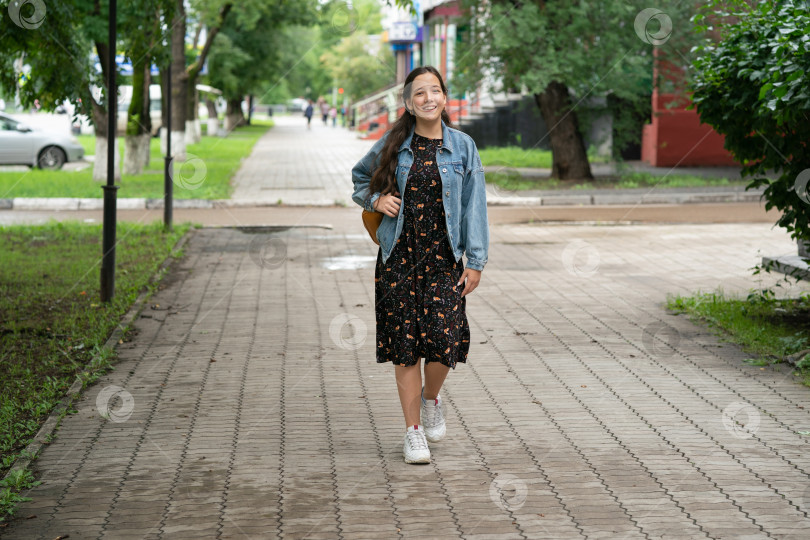 Скачать девочка в платье и джинсовой куртке с оранжевым рюкзаком за плечами идет в школу. фотосток Ozero