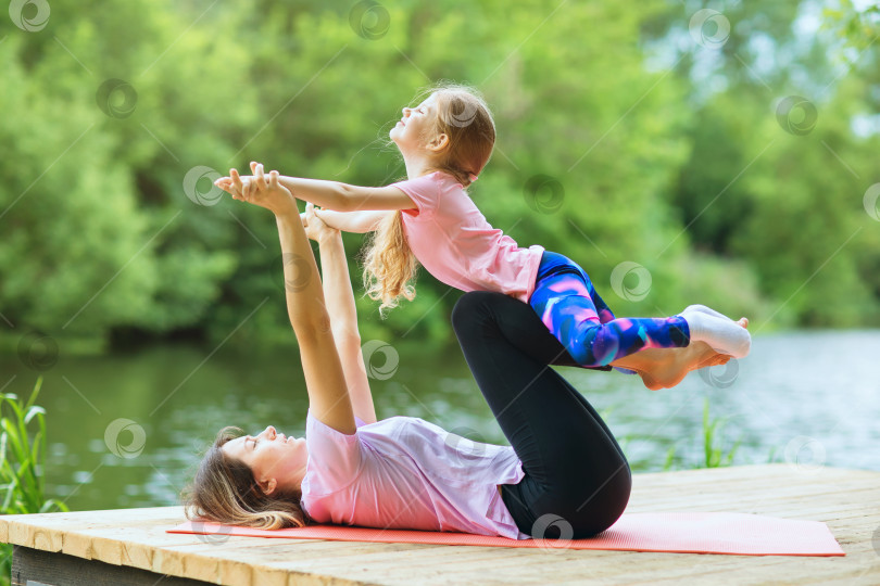 Скачать Мама и дочь выполняют упражнение йоги на берегу реки теплым солнечным днем, концепция здорового образа жизни фотосток Ozero