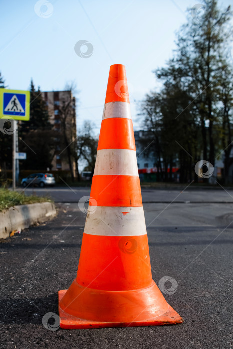Скачать Ярко-оранжевый дорожный конус, стоящий на дороге. Вертикальная фотография фотосток Ozero
