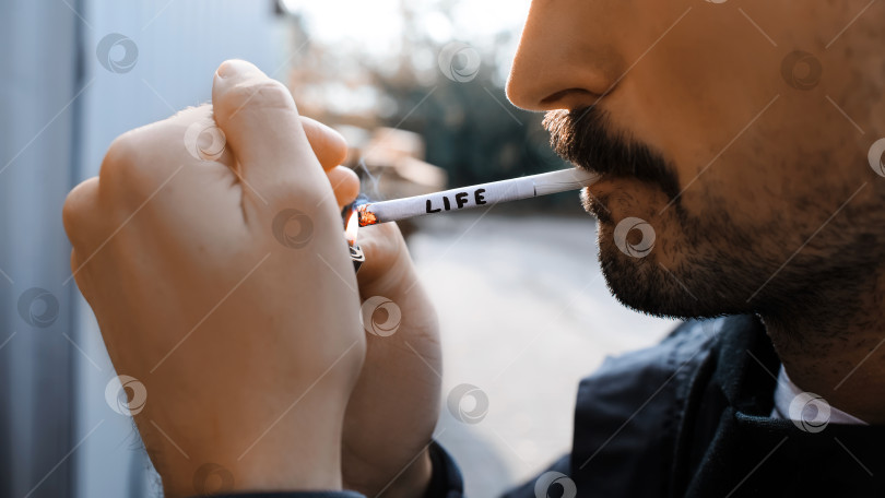 Скачать Мужчина закуривает сигарету на открытом воздухе, снимая крупным планом.Текст о сигаретной ЖИЗНИ. Концепция "Не кури, сигарета убивает" фотосток Ozero