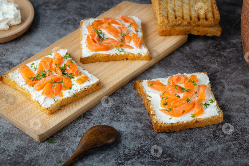 Скачать Домашний хлеб на деревянной разделочной доске с творожным сыром, лососем и зеленью фотосток Ozero