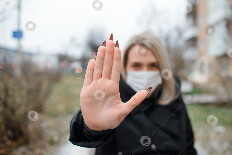 Скачать Молодая женщина в медицинской маске для лица показывает жест остановки. Портрет девушки на улице зимой, выборочный фокус на руке фотосток Ozero