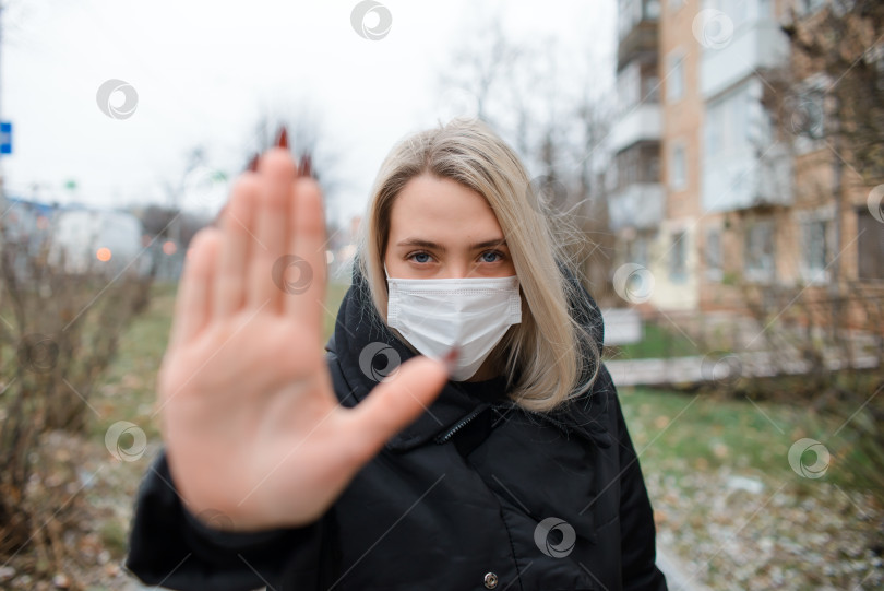 Скачать Молодая женщина в медицинской маске для лица показывает жест остановки. Портрет девушки на улице зимой, выборочный фокус на лице фотосток Ozero