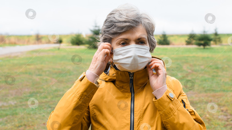 Скачать Портрет пожилой женщины, снимающей с лица медицинскую маску. Пожилая женщина в защитной маске на улице в холодную погоду. фотосток Ozero