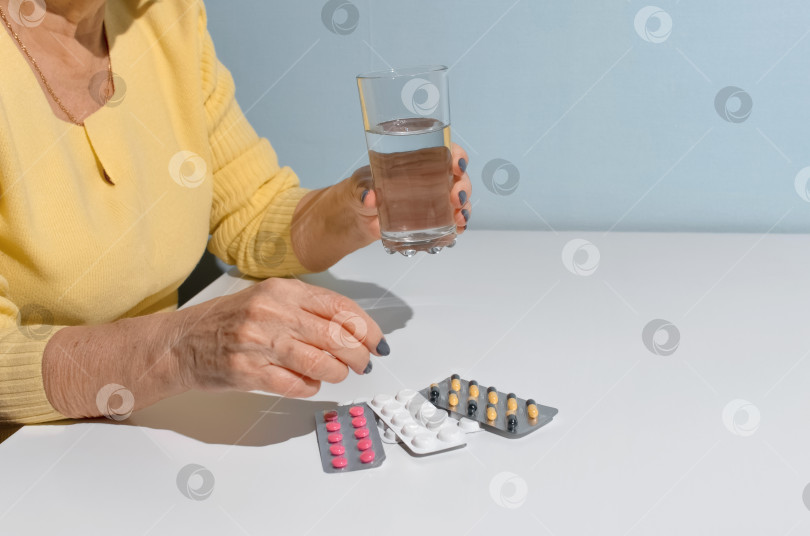 Скачать Пожилая женщина принимает лекарства. Крупным планом женские руки, держащие стакан с водой и таблетки. Концепция лечения, выход на пенсию по болезни фотосток Ozero
