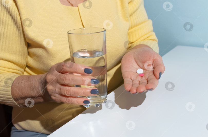 Скачать Пожилая женщина пьет таблетки. Крупным планом женские руки, держащие стакан с водой и лекарством. Концепция лечения, выход на пенсию по болезни фотосток Ozero