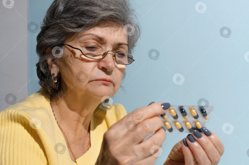 Скачать Пожилая женщина в очках пытается прочитать инструкцию к лекарственным таблеткам, крупный план. Концепция лечения, выход на пенсию по болезни фотосток Ozero