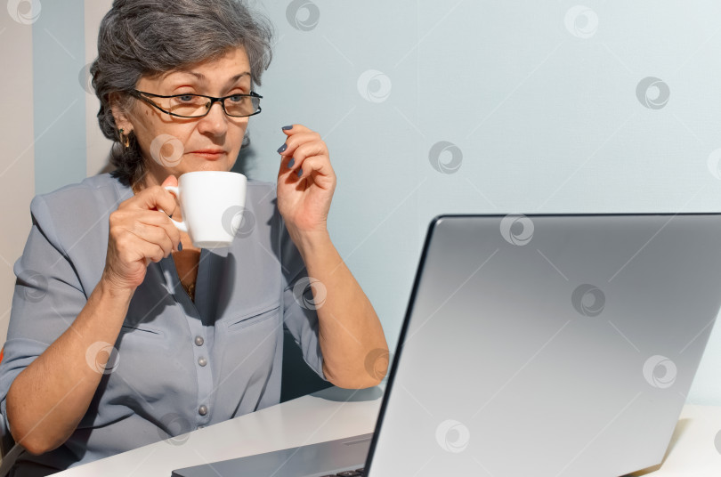 Скачать Пожилая женщина пьет кофе и удивленно смотрит на ноутбук. фотосток Ozero