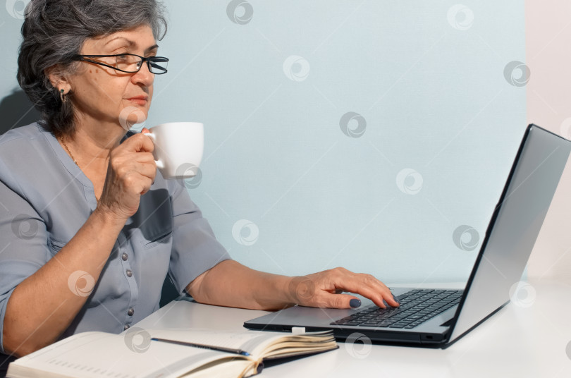 Скачать Пожилая женщина в очках учится онлайн дома. Женщины пьют кофе и пользуются ноутбуком. Концепция удаленной работы, фриланса, работы на пенсии фотосток Ozero