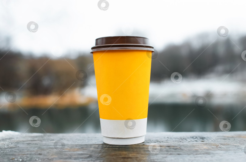 Скачать Чашка кофе, стоящая на деревянном столе на открытом воздухе, крупным планом. Желтое бумажное стекло на зимнем фоне. фотосток Ozero