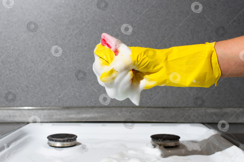 Скачать Женская рука в перчатке чистит газовую плиту. Женщина выжимает пену из губки. Уборка кухни, домашние дела фотосток Ozero