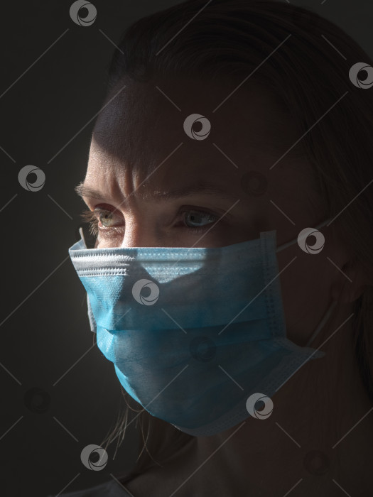 Скачать Женщина на темном фоне носит медицинскую одноразовую маску, чтобы избежать заражения вирусами фотосток Ozero