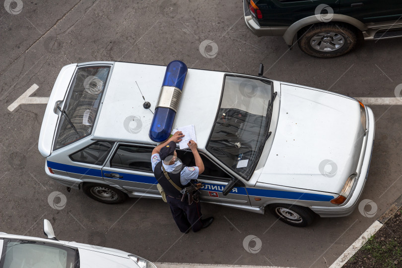 Скачать Полицейский делает запись, облокотившись на крышу автомобиля. Вид сверху. Москва, Россия фотосток Ozero