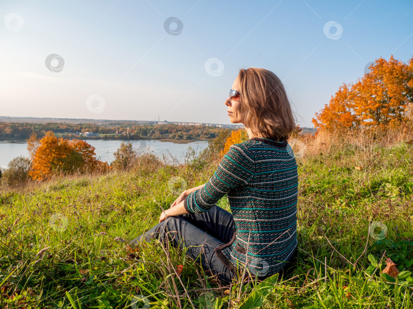 Скачать Активная элегантная женщина средних лет, сидящая осенью на холме с прекрасным видом фотосток Ozero