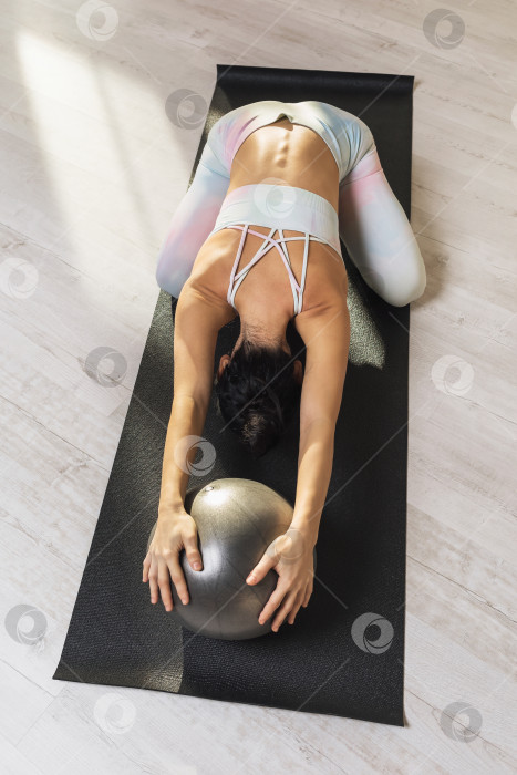 Скачать Женщина, практикующая йогу, выполняет упражнение баласана с мячом, поза ребенка, тренируется на коврике в студии фотосток Ozero