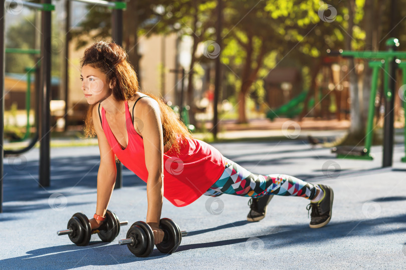 Скачать Девочка-спортсменка выполняет упражнения с гантелями на детской площадке теплым солнечным утром. Концепция здорового образа жизни фотосток Ozero