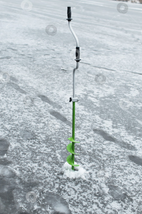 Скачать Дрель, стоящая на замерзшем озере. Снаряжение для зимней рыбалки, бурение лунок. фотосток Ozero