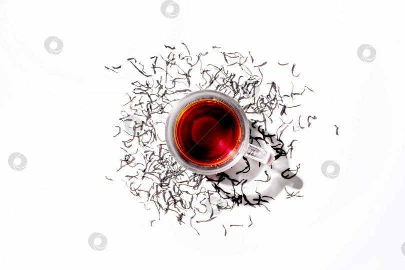 Скачать Стеклянная чашка с черным чаем и рассыпанными сухими листьями цейлонского чая, вид сверху фотосток Ozero