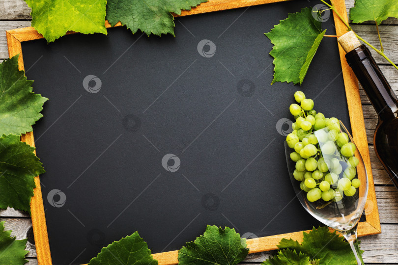 Скачать Полная бутылка вина с бокалом, гроздью винограда и листьями на деревянном столе с местом для копирования, вид сверху фотосток Ozero