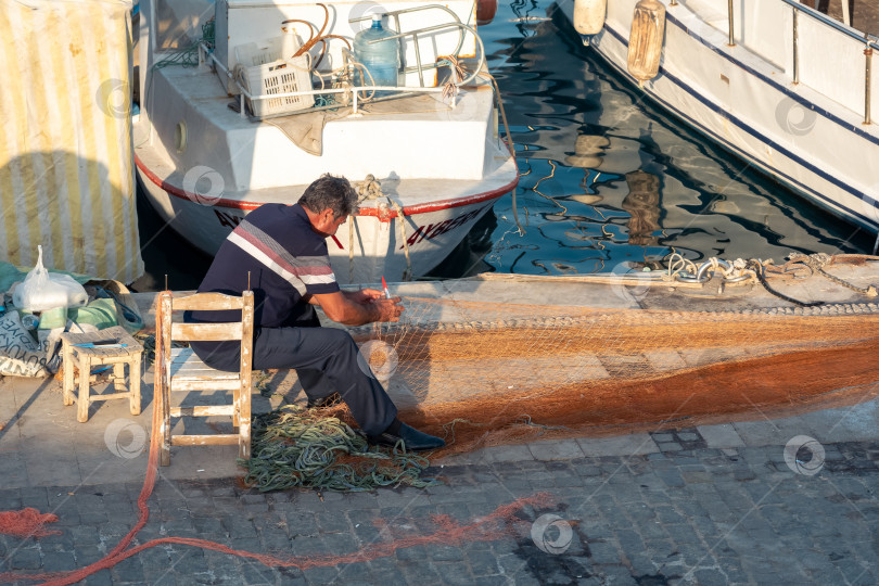 Скачать рыбак чинит свою сеть на причале старой гавани в Анталии фотосток Ozero
