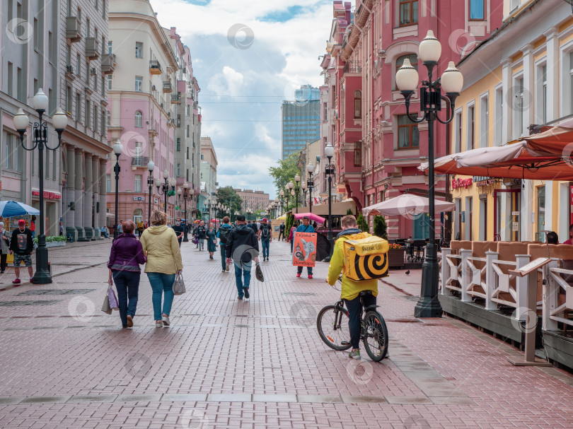 Скачать Доставка еды. Велосипедист развозит еду по улице Арбат в Москве. фотосток Ozero