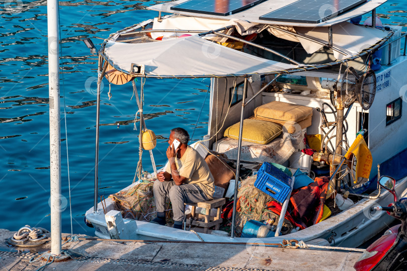 Скачать моряк разговаривает по телефону, сидя на своей рыбацкой лодке, пришвартованной у пирса фотосток Ozero