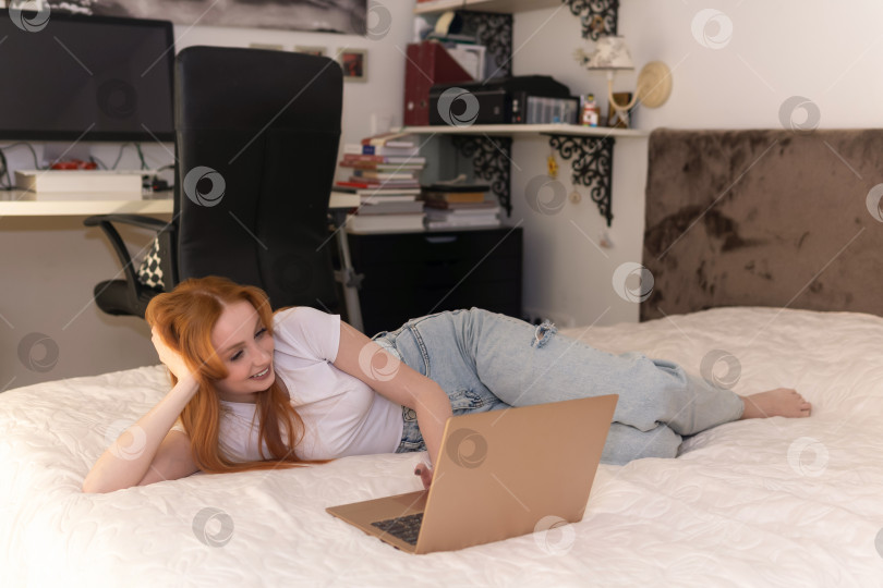 Скачать молодая женщина, лежащая с ноутбуком на кровати дома фотосток Ozero