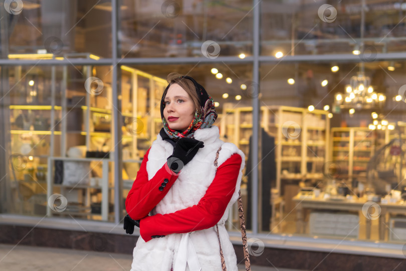 Скачать молодая женщина в платке на голове в холодную погоду стоит снаружи на фоне размытой яркой витрины магазина фотосток Ozero