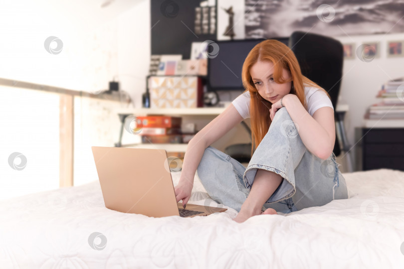 Скачать молодая женщина сидит с ноутбуком на кровати дома фотосток Ozero