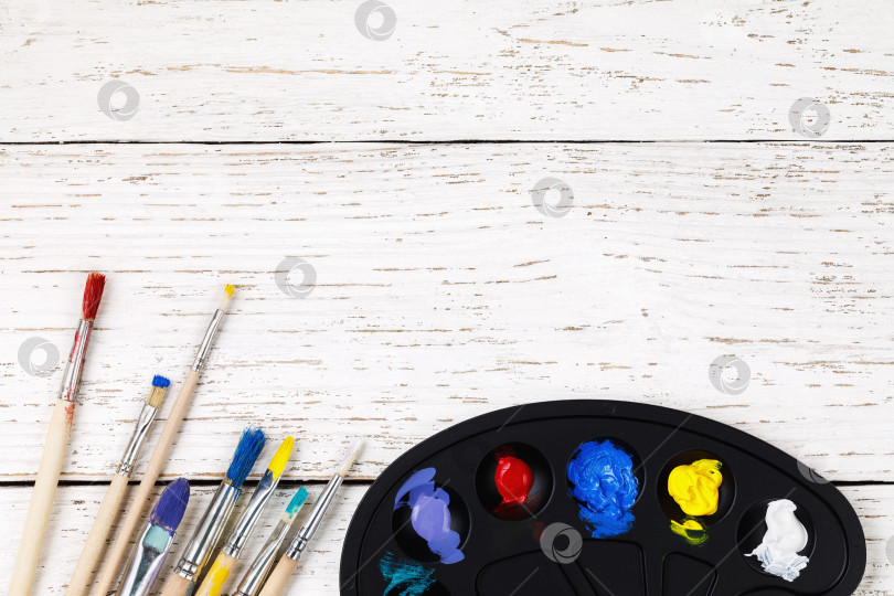 Скачать Художественные принадлежности: палитра с красками и кисточками для рисования на деревянном столе с местом для текста, вид сверху фотосток Ozero