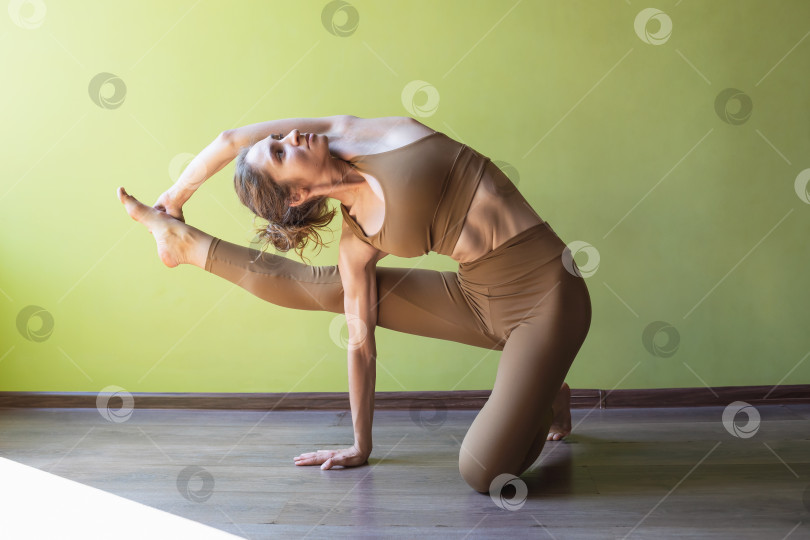 Скачать Молодая женщина, практикующая йогу, выполняющая упражнение Ардха Вишвамитрасана, поза мудреца, тренирующаяся в спортивной одежде в комнате у стены фотосток Ozero