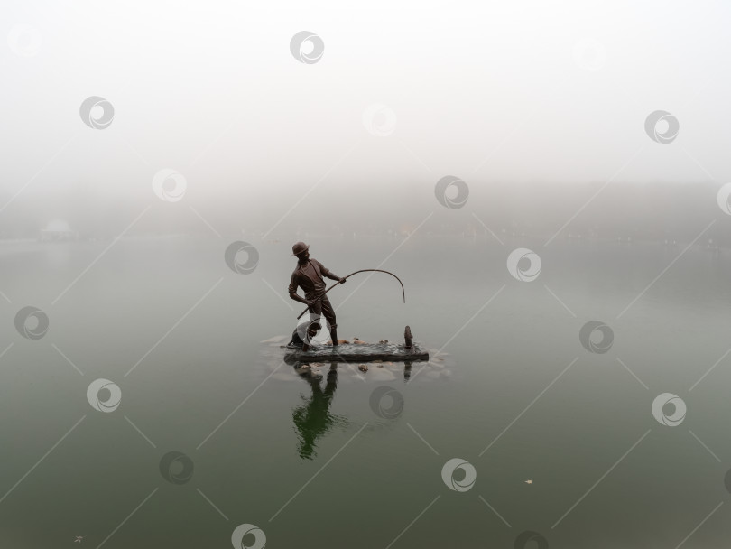 Скачать Скульптура "Рыбак и кот-рыболов" на туманном городском озере. фотосток Ozero