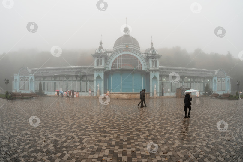 Скачать Мягкий фокус. Железноводская пушкинская галерея туманной осенью. Люди прогуливаются под зонтиками. фотосток Ozero